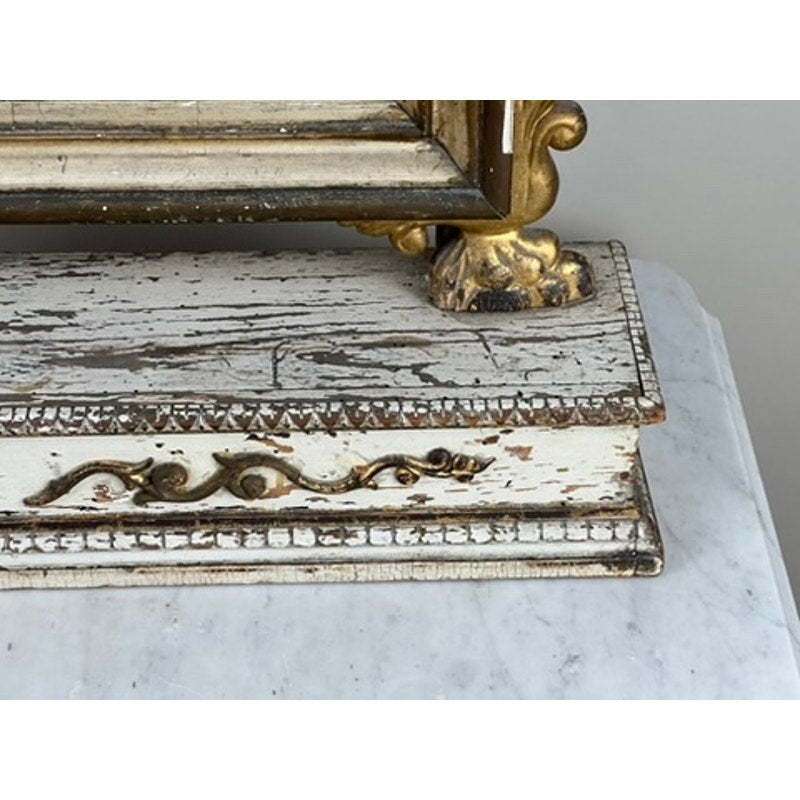 A close-up of a distressed gilt wood pedestal with chipped white paint and gold accents, part of an Antique French Empire Vanity or Table Mirror c. Mid 19th Century, resting on a marble surface. Brand: Unknown.