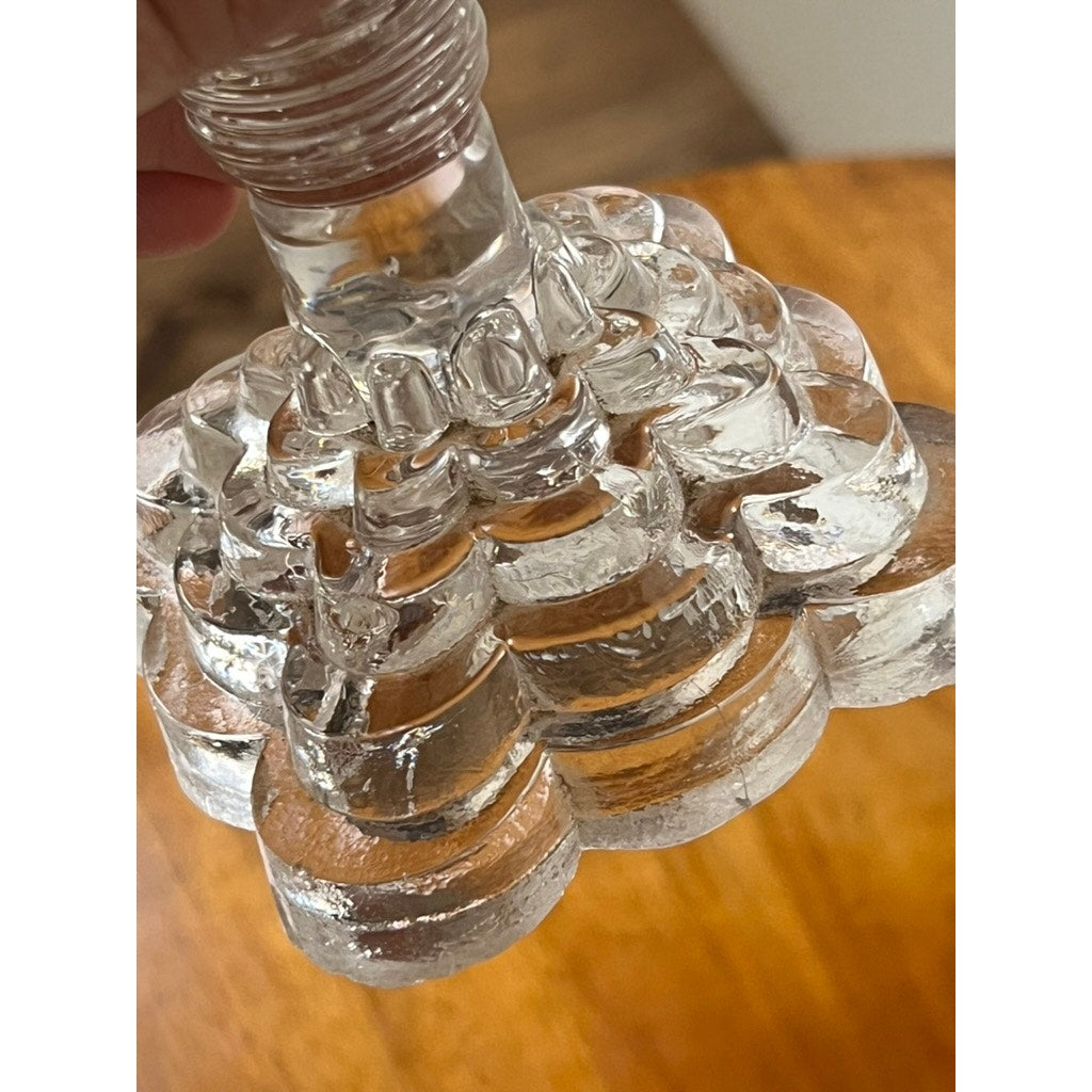 Close-up of a clear glass object with a textured, scalloped base, likely an Attributed Boston & Sandwich Pressed Glass Boudoir Fluid Lamp, circa 1850, held above a wooden surface.