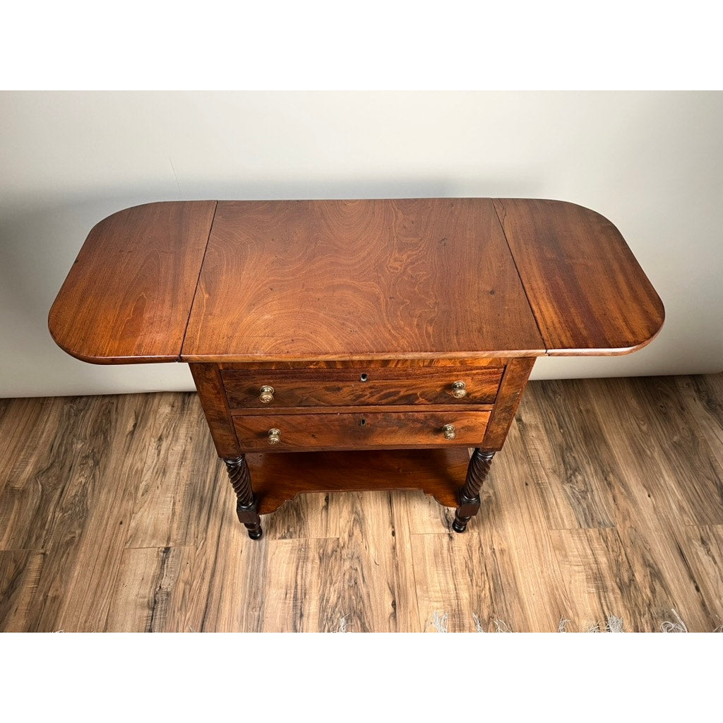 Antique Federal Mahogany Two Drawer Work Stand c. 1820 with lions head pulls, featuring drop-leaf sides and turned legs, shown on a wooden floor against a plain white wall. Brand: None/Unknown.