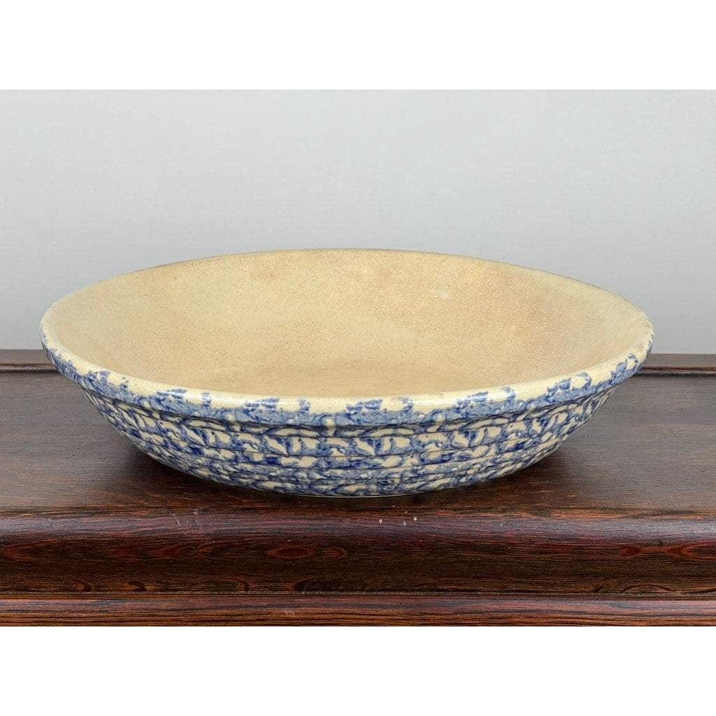 The Robinson Ransbottom Roseville Blue Spongeware Pasta Bowl by Robinson Ransbottom features a beige interior and a textured blue and beige exterior, reminiscent of vintage American stoneware, displayed on a dark wood surface against a light background.