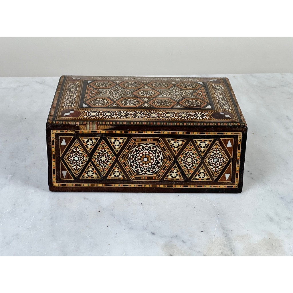 An Antique Persian (likely Syrian) Khatam inlaid wood secret drawer jewelry box from the late 19th century, featuring intricate brown, white, and black geometric patterns, is displayed on a white marble surface against a light background.
