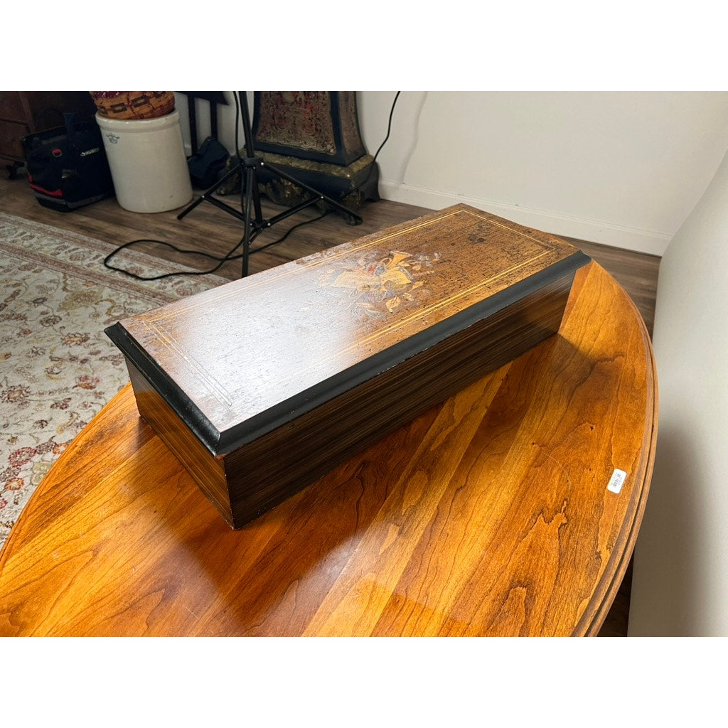 An Antique Swiss 12 Tune Music Box, c. Late 19th Century, with decorative inlay rests on a polished wooden table in a room featuring a patterned rug and assorted furnishings. Brand unknown.