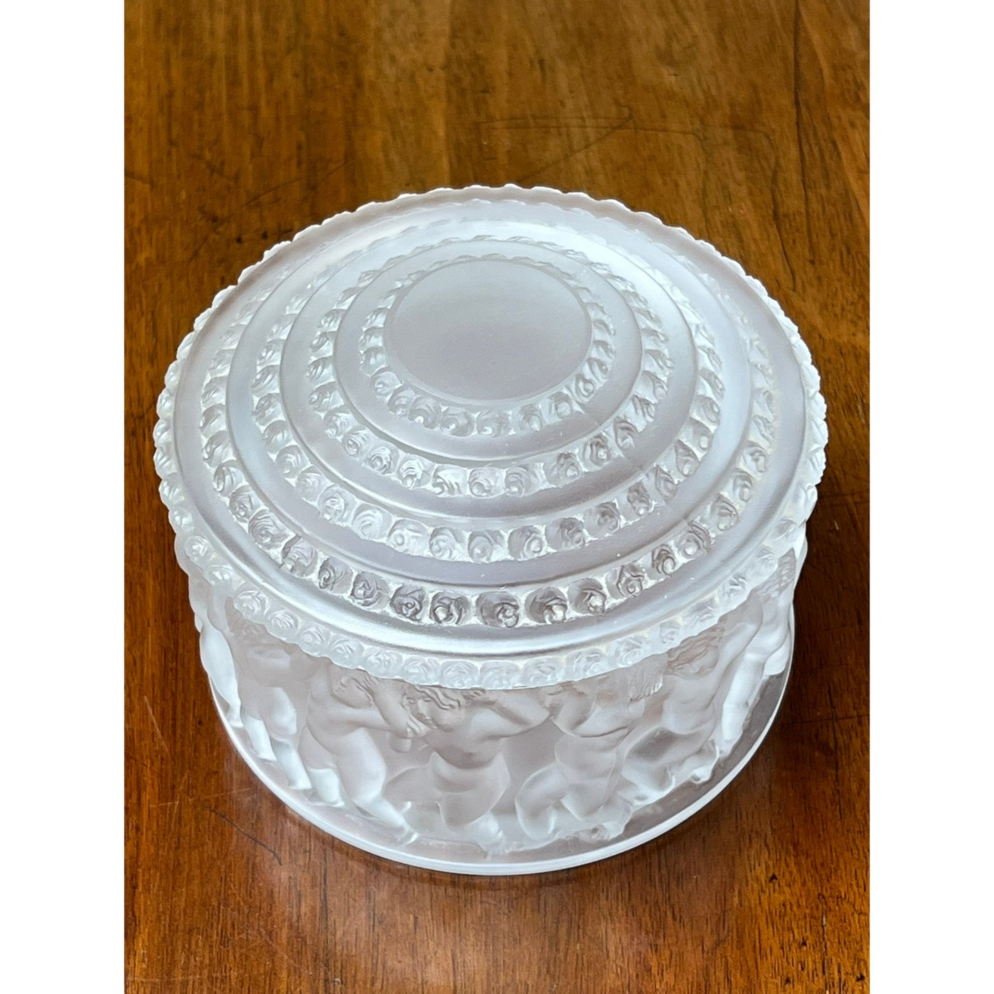 The Vintage Lalique Crystal Enfants Box by Lalique features a frosted glass finish and textured lid, with the iconic embossed Enfants pattern of dancing figures adorning its sides.