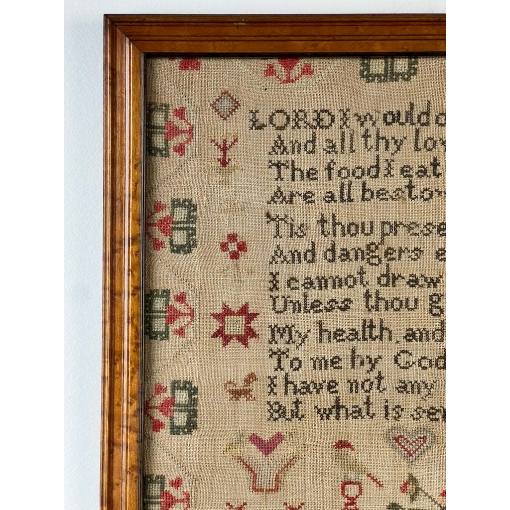 A close-up of a framed, vintage embroidered sampler with faded green and red patterns and partial text stitched in black thread on beige fabric, reminiscent of the Exceptional English Regency Schoolgirl Needlework Sampler by Charlotte Rees, age 11, dated 1816.
