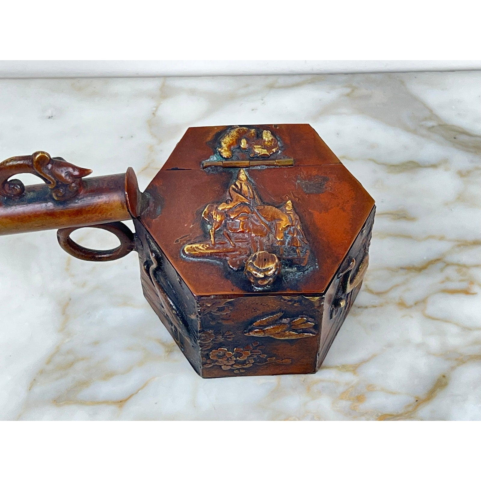 An Antique Meiji Period Japanese Bronze Yatate Inkwell, hexagonal with embossed designs and a cylindrical handle, sits on a white marble surface. No brand name; features latch and bronze-toned finish reminiscent of classic yatate writing sets.