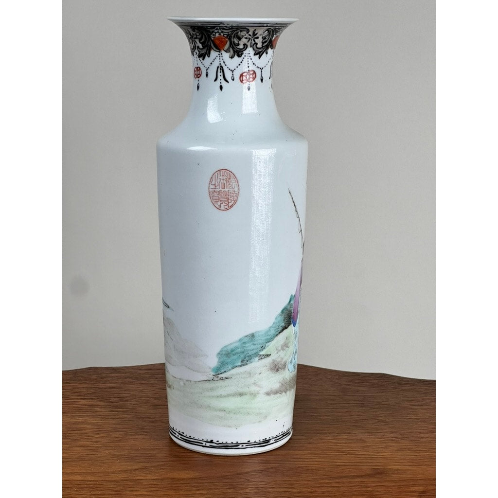 An Antique Qing Dynasty Famille Rose 12” Vase with Qianlong mark, featuring delicate painted scenes in soft colors with black and red rim patterns, stands on a wooden surface. Brand: None/Unknown.