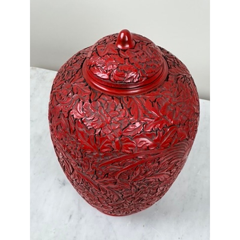 An Antique Chinese Hand-Carved Cinnabar Lacquered Lidded Jar, probably Qianlong, with intricate floral and foliage patterns is displayed on a white marble surface against a plain light background.