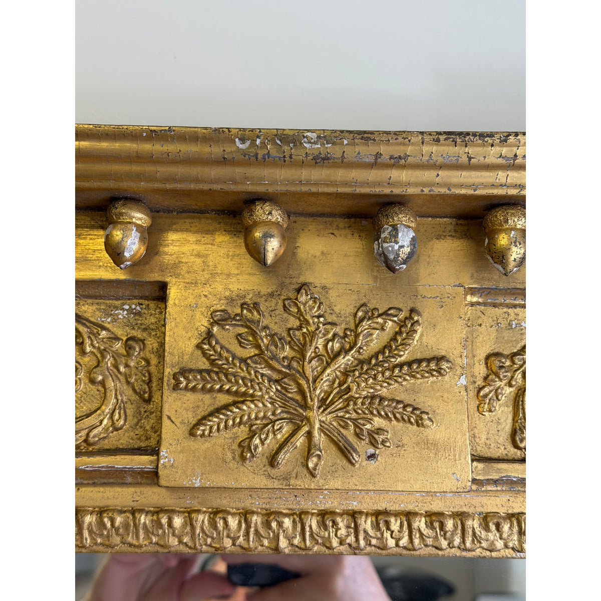 Detail of an American Federal Giltwood Pier Mirror, Possibly Massachusetts or New York, circa 1815–1830, featuring an antique giltwood frame with a central relief of wheat stalks and a row of acorn finials along the top edge.