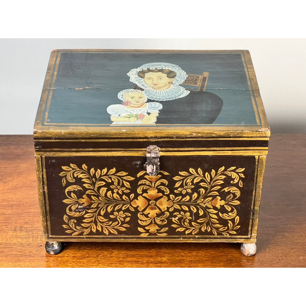 An Antique New England Folk Art Painted Portrait Document Box, Mother & Child, c. 1840–1860, with gold floral designs and a lid featuring a woman in a bonnet holding a child, is displayed on a wooden surface. Brand: None/Unknown.