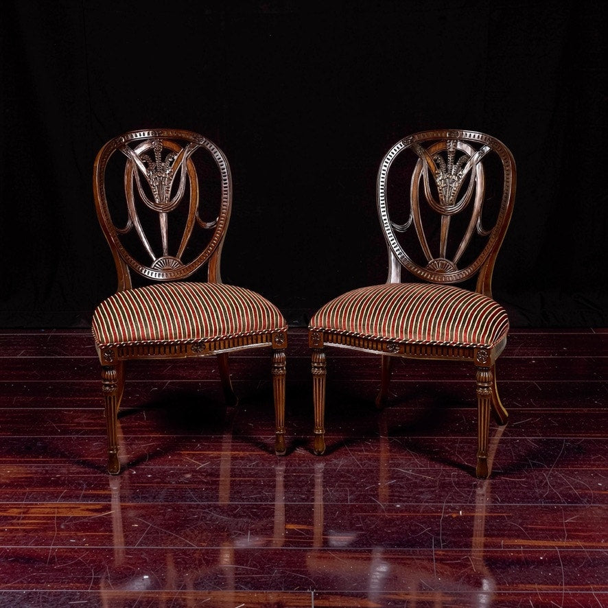 A vintage pair of Ardley Hall wheel back side chairs with elegant carved backs and striped red, white, and gold upholstery highlight classic English design against a glossy dark wood floor and black backdrop.