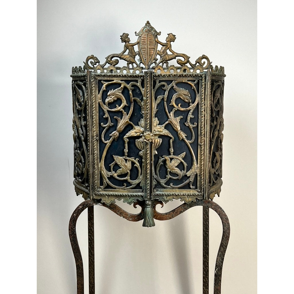 An Antique Gothic Revival cast iron and brass phone stand, attributed to Oscar Bach or Bertram Segar c. 1920 Greenwich Village, features ornate detailing and a decorative crest atop curved legs, set against a plain light background.