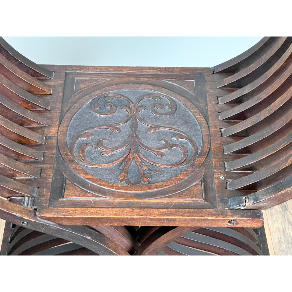 Close-up of an Antique Italian Renaissance Walnut Savonarola Chair (late 19th c.) seat, featuring a carved circular leaf and vine motif, curved slats, and a rich dark walnut finish. Brand: None/Unknown.