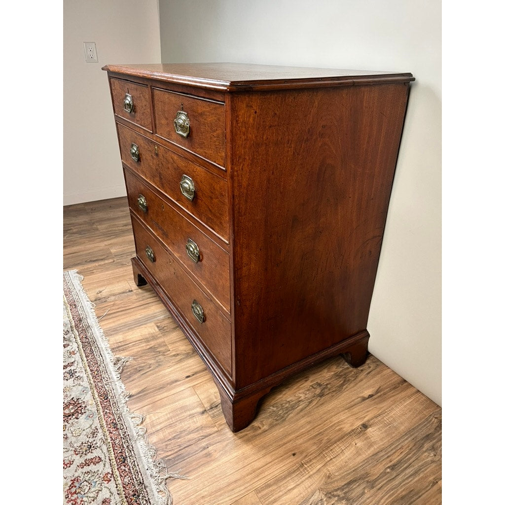 A Late Georgian English Mahogany Chest of Drawers, Circa 1780–1810, stands on a wood floor next to a patterned rug and an off-white wall.