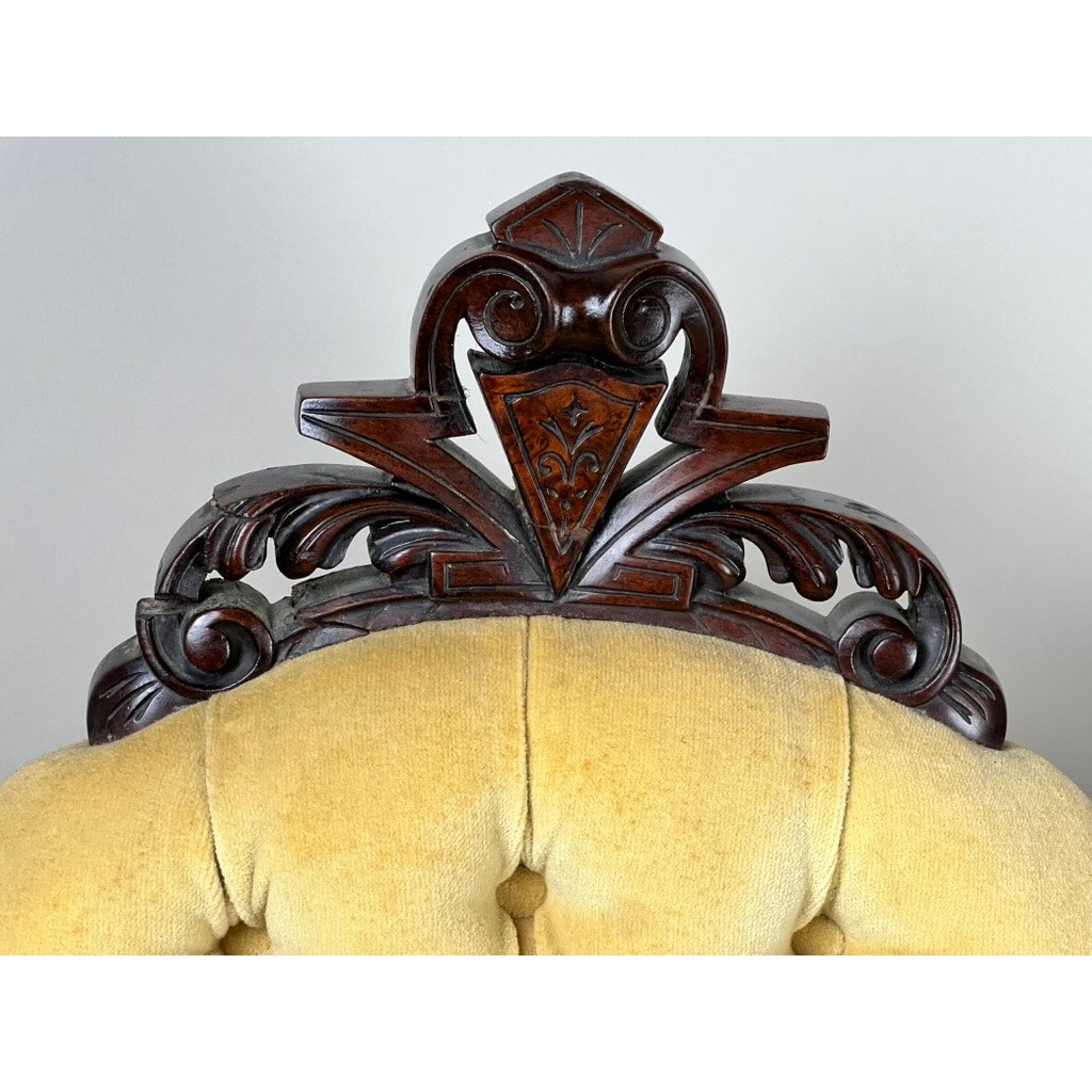 Close-up of an ornate walnut chair back with intricate scrollwork and a central motif over a tufted yellow cushion—part of a fine antique pair of Renaissance Revival side chairs attributed to John Jelliff, Newark, circa 1880.