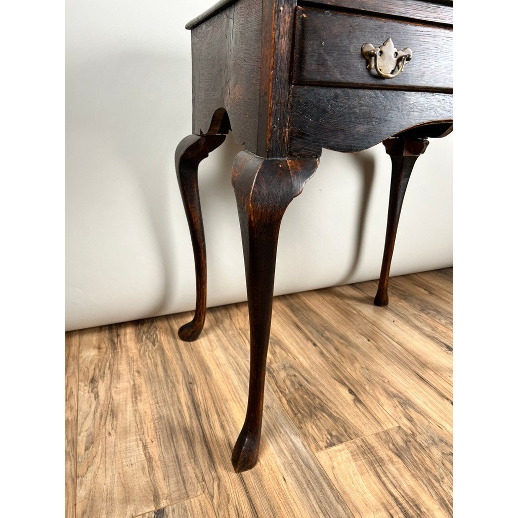 Close-up of the dark wooden legs and lower drawer of an Antique Queen Anne Style George III Oak One Drawer Stand (late 18th c.), featuring curved cabriole legs, set on a wood-patterned floor against a plain light wall.