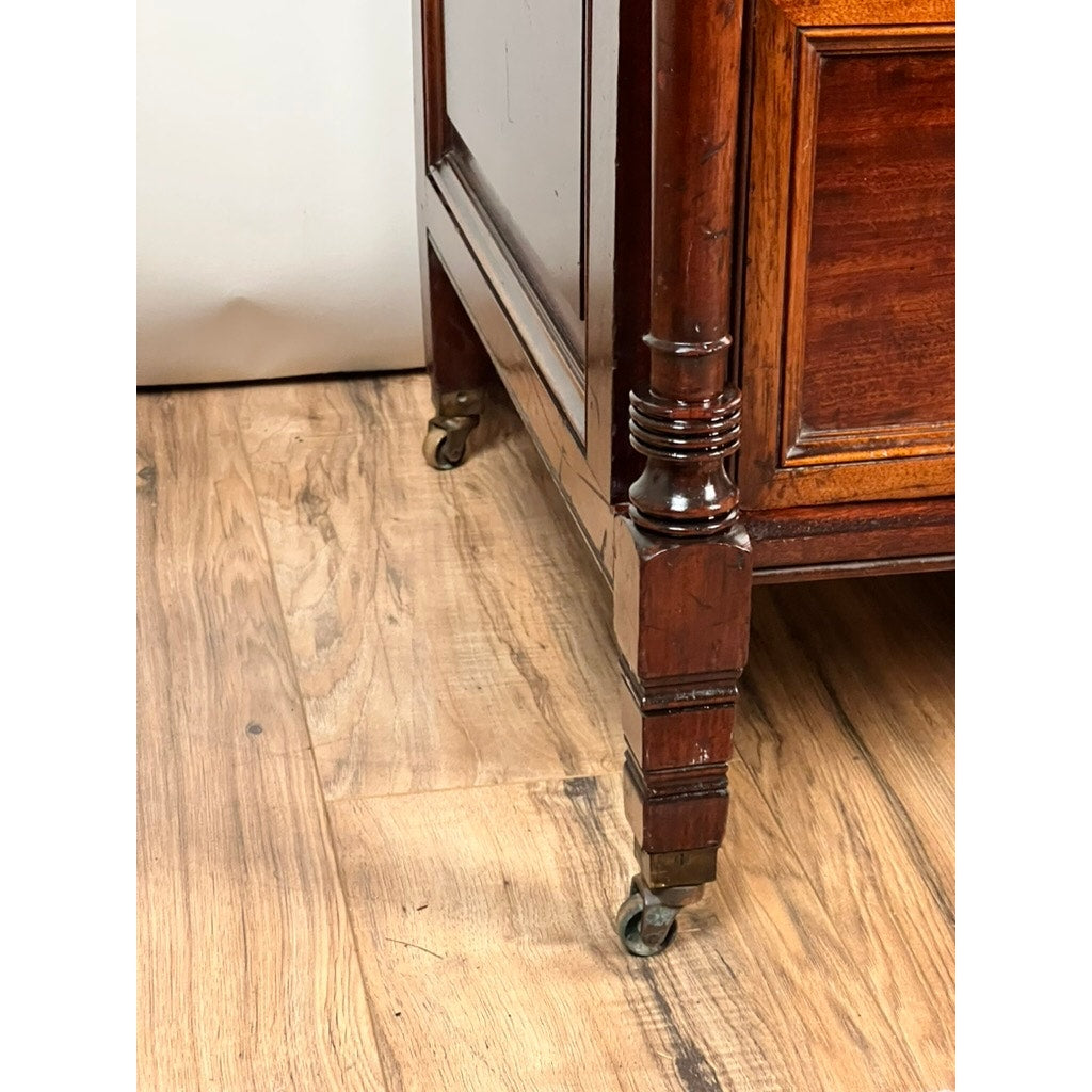 Close-up of a decorative carved wooden leg with metal caster on a light hardwood floor, from an Antique Victorian Aesthetic Movement Mahogany Four Over Four Gentlemen’s Chest c. 1880. Brand: Unknown.