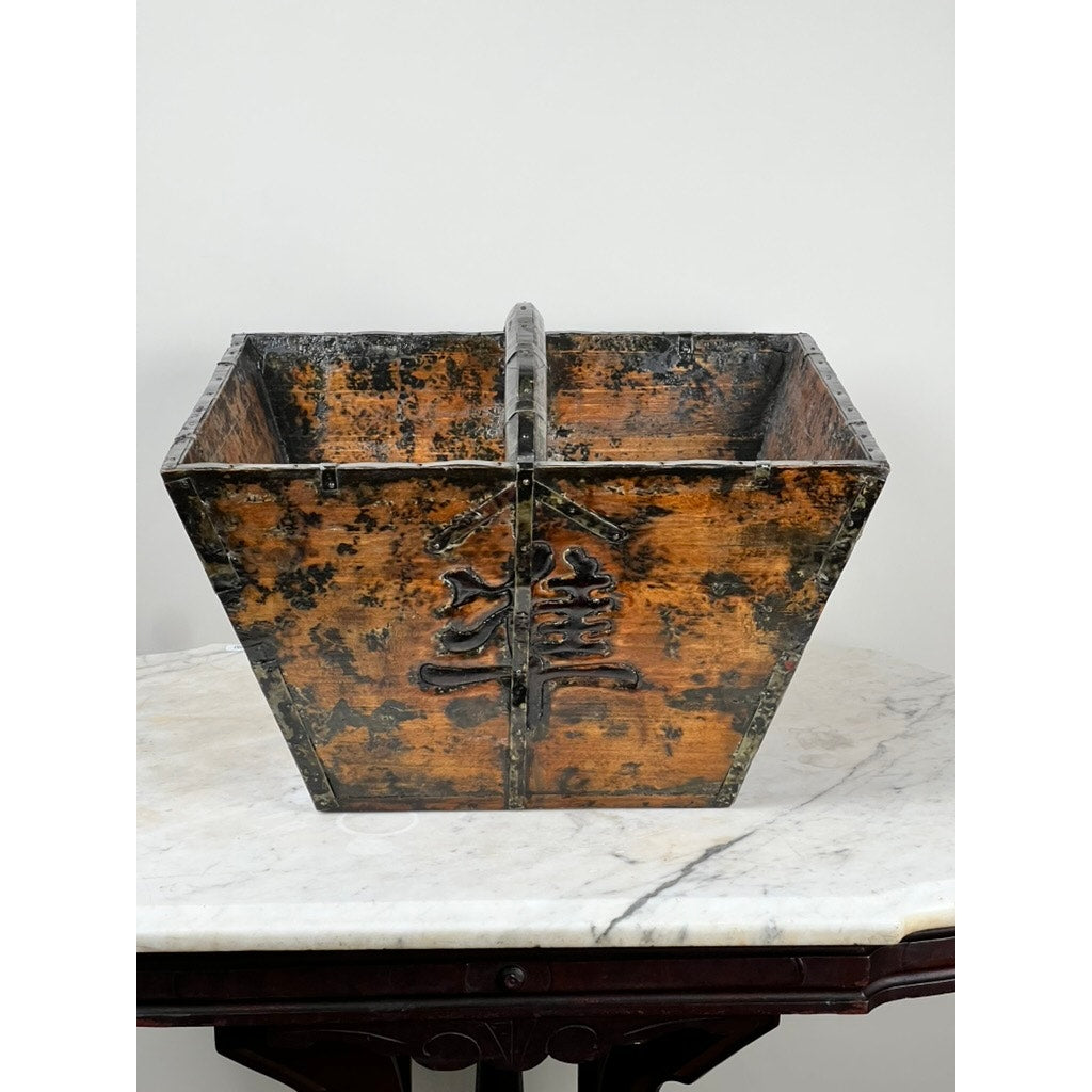 An Antique Chinese Elm Dou Rice Measure, likely from Shanxi, mid-19th century, with a weathered brown finish and black edges, sits on a white marble tabletop featuring Asian-inspired engraved characters.