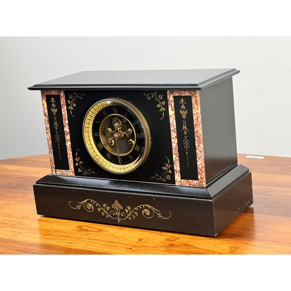An Antique Victorian Slate Mantle Clock with Open Escapement 8 Day Time and Strike (late 19th c.), accented with gold and pink marble, rests on a polished wood surface against a plain light background. Brand: None/Unknown.