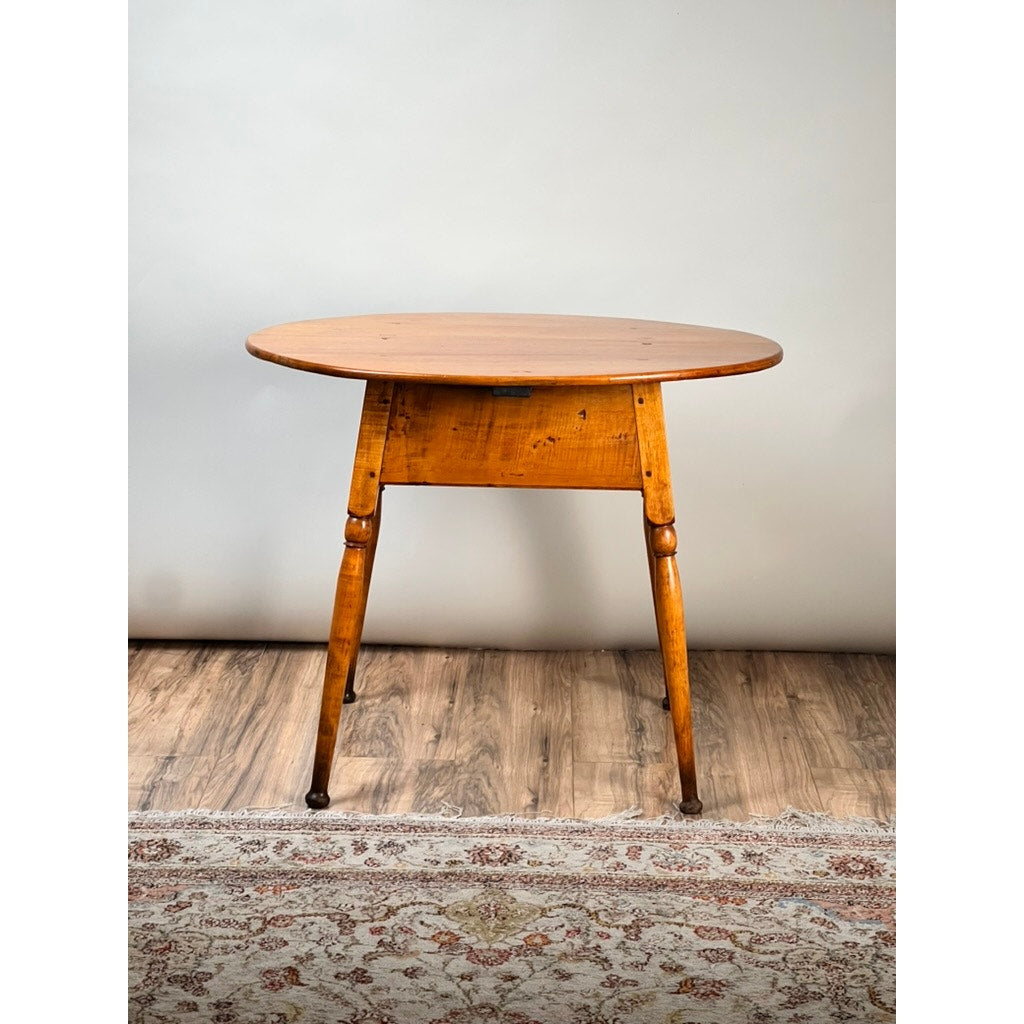 An Antique American Queen Anne Maple Tavern Table (New England, circa 1760–1790) stands on a wood floor over a patterned rug, its simple rustic design set against a plain light-colored wall.