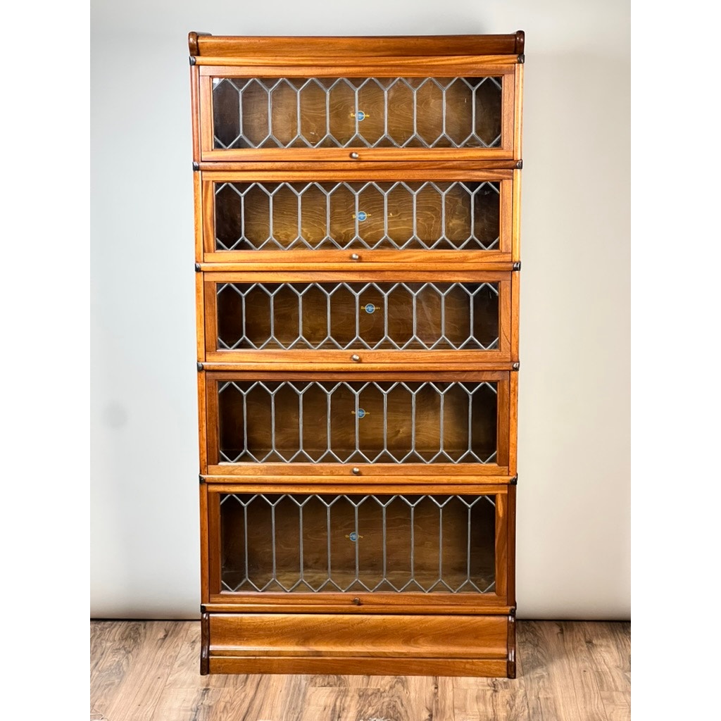The Globe Wernicke Vintage Leaded Glass Five Stack Barrister Bookcase features five shelves with geometric leaded glass doors, echoing classic design. It stands on a wooden floor against a light-colored wall.