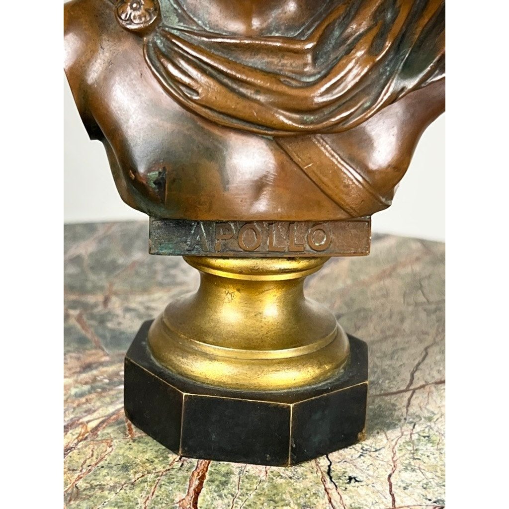 An antique small bronze “Apollo Belvedere” with a Vienna foundry mark sits atop a gold and black pedestal on a marbled surface.