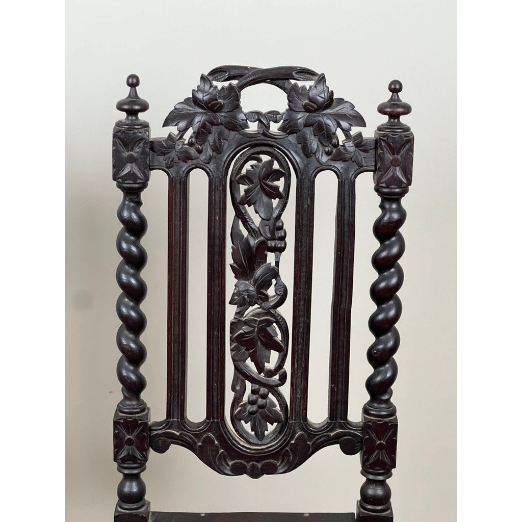 An ornate backrest from a pair of antique French walnut hunting chairs (late 19th century), featuring intricate floral carvings and twisted spindle columns, set against a plain light background. Brand: Unknown.