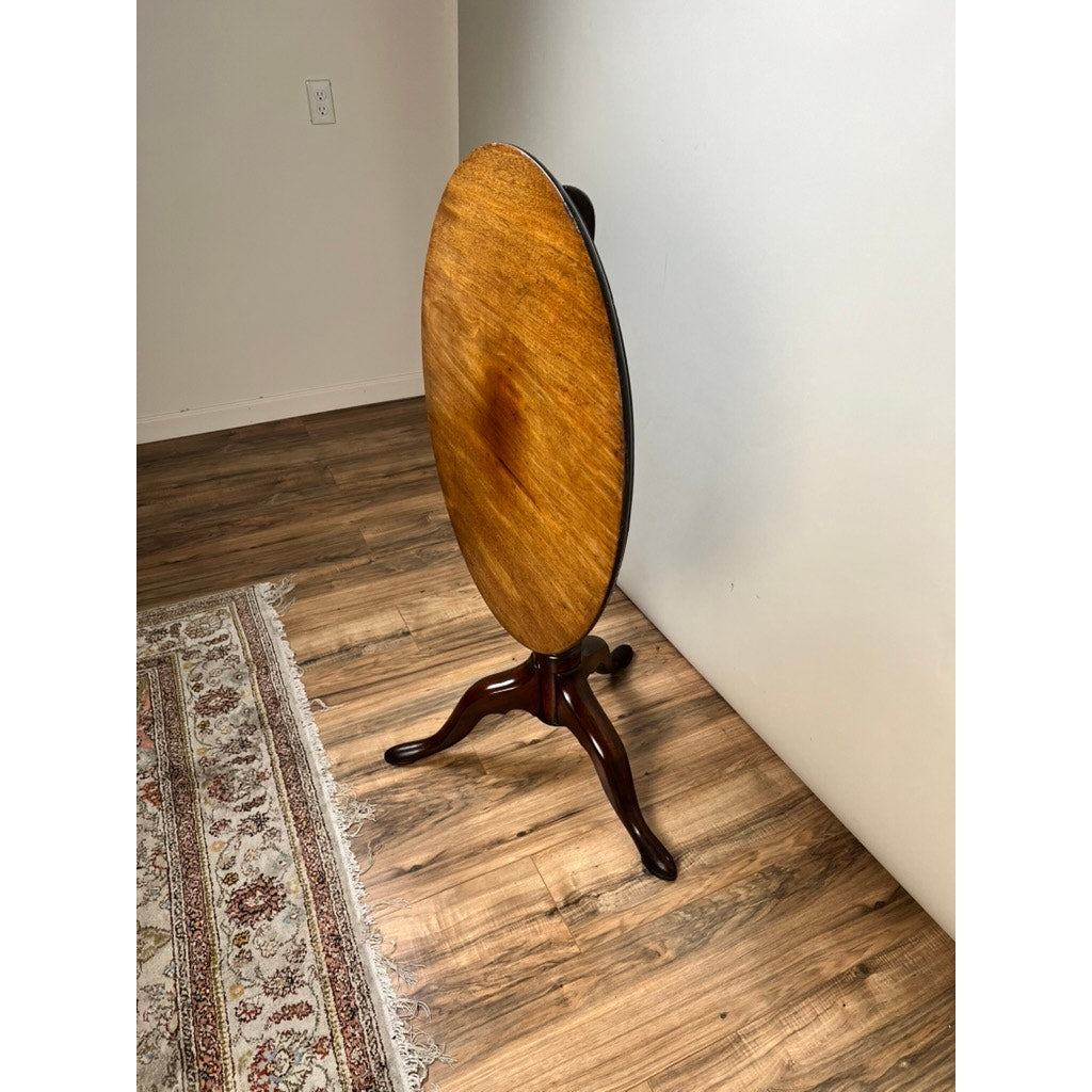 An Antique Queen Anne Mahogany Birdcage Tilt Top Breakfast Table (early 19th c.) stands flipped vertically against a white wall on a hardwood floor, next to a patterned rug. Brand: None/Unknown.