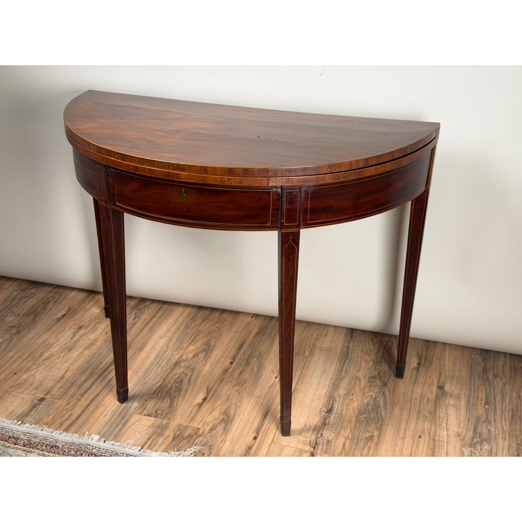 An English George III Mahogany and Satinwood-Inlaid Demilune Games Table, circa 1790–1810, featuring a half-moon top and thin, tapered legs.
