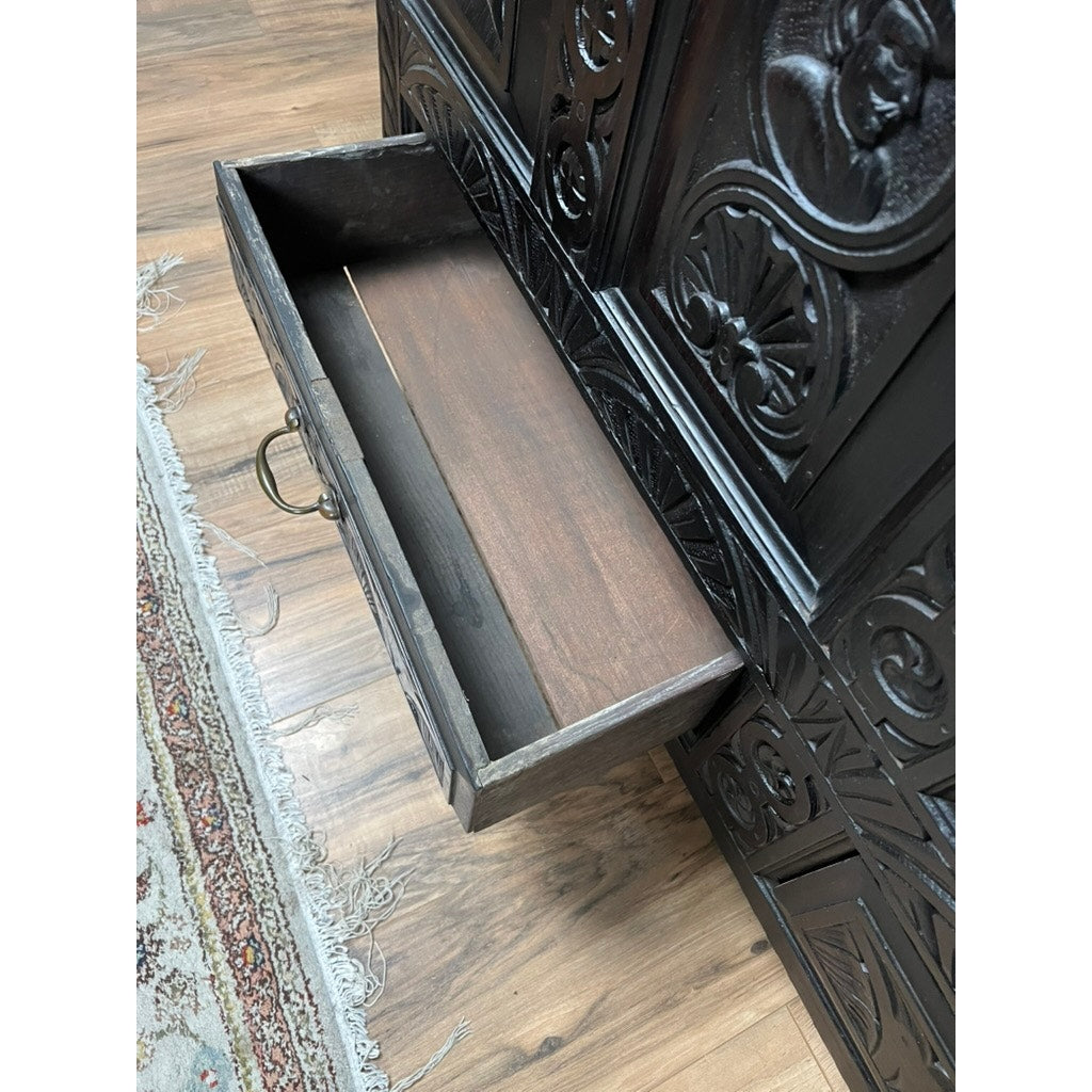 An Antique 18th Century Charles II Style Mule Chest, possibly Irish or Scottish, features dark wood, ornate carvings, and an open drawer showing a spacious interior. A patterned rug and wooden floor are visible beside the chest. Brand: None/Unknown.