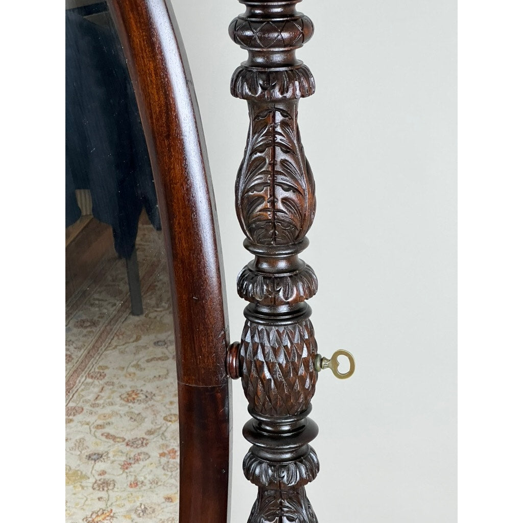 A close-up of the Impressive Antique American Empire Acanthus and Barbola Rose Carved Cheval Mirror c. 1840, showing ornate carvings and a brass key, with a patterned rug and partial wooden bed frame in the background.