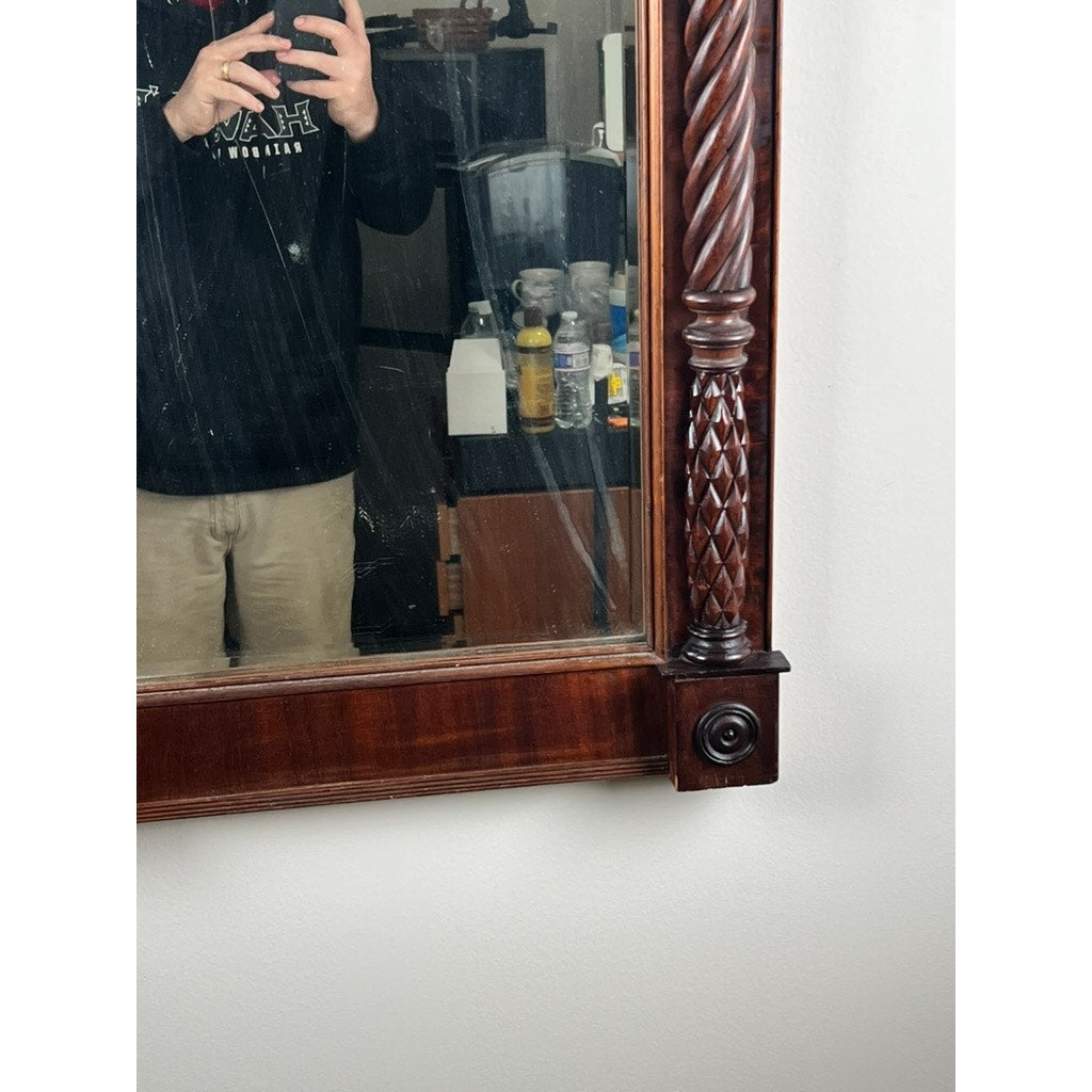 A person in a black shirt and khaki pants is partially visible in the reflection of an Antique American Empire Mahogany Pier Mirror c. 1840, with bottles and assorted items seen on a cluttered surface behind them.