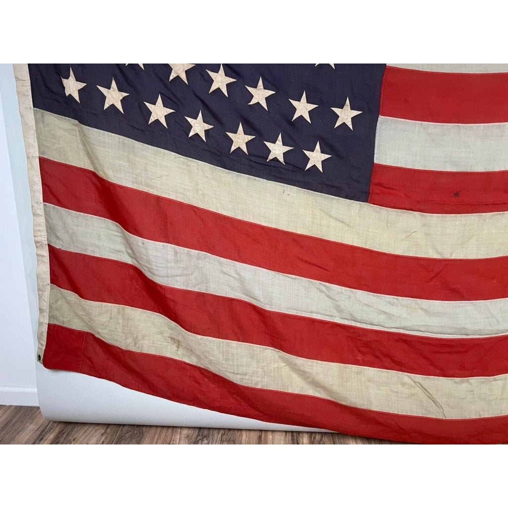 An Antique 45 Star American Flag from the Spanish–American War era (9’9 x 6) with worn, faded fabric is draped against a wall, partially visible and evoking its historic past. Brand: None/Unknown.