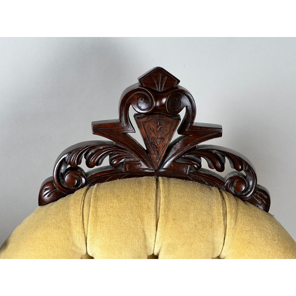 Close-up of the ornate crest on a Fine Antique Pair Renaissance Revival Walnut Side Chair, attributed to John Jelliff (Newark, c. 1880), showing intricate carvings above a light yellow upholstered tufted backrest.