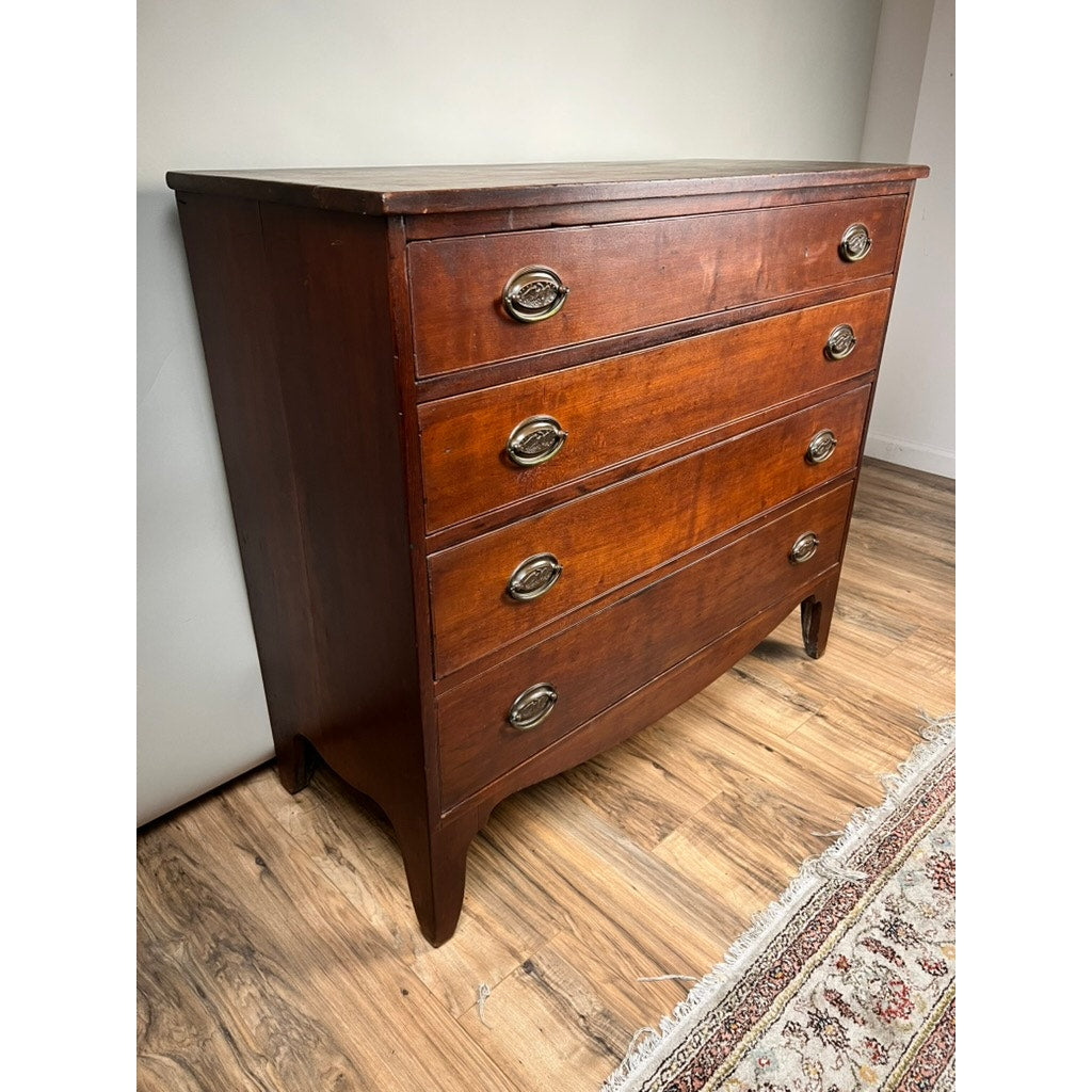 A rare labeled William Lloyd Springfield Massachusetts Federal cherry chest of drawers, circa 1800, features four drawers with two oval brass handles each. This elegant wooden dresser sits on a wooden floor beside a patterned rug and a white wall.