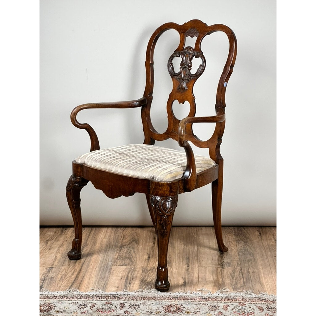 An Antique George III Mahogany Open Arm Chair (late 18th century) with ornate carvings, curved armrests, and a striped cushioned seat is placed on a wooden floor near a patterned rug. Brand: None/Unknown.