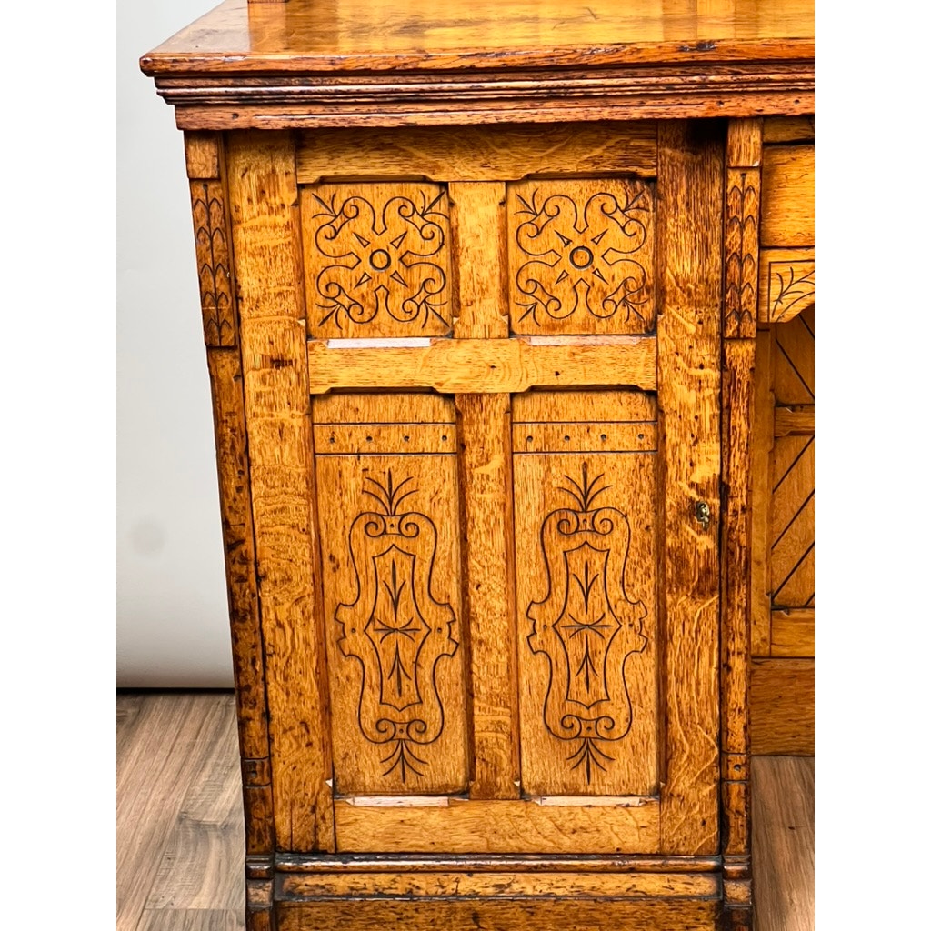 Close-up of a wooden cabinet with detailed carved and engraved door panels reminiscent of an Antique Victorian Aesthetic Movement Oak Desk in Original Finish from the late 19th century, with a warm brown hue and visible wood grain.
