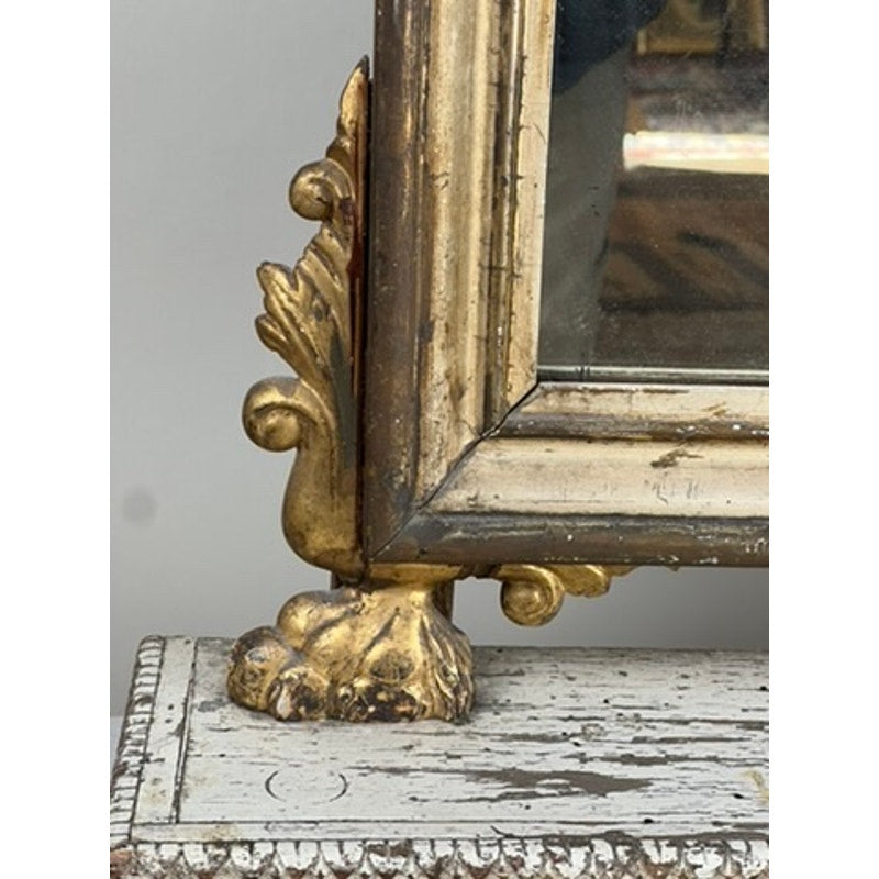 A close-up of an ornate, gold-painted foot and frame from an Antique French Empire Gilt Wood Vanity or Table Mirror (c. Mid 19th Century), resting on a distressed, chipped white wooden surface.