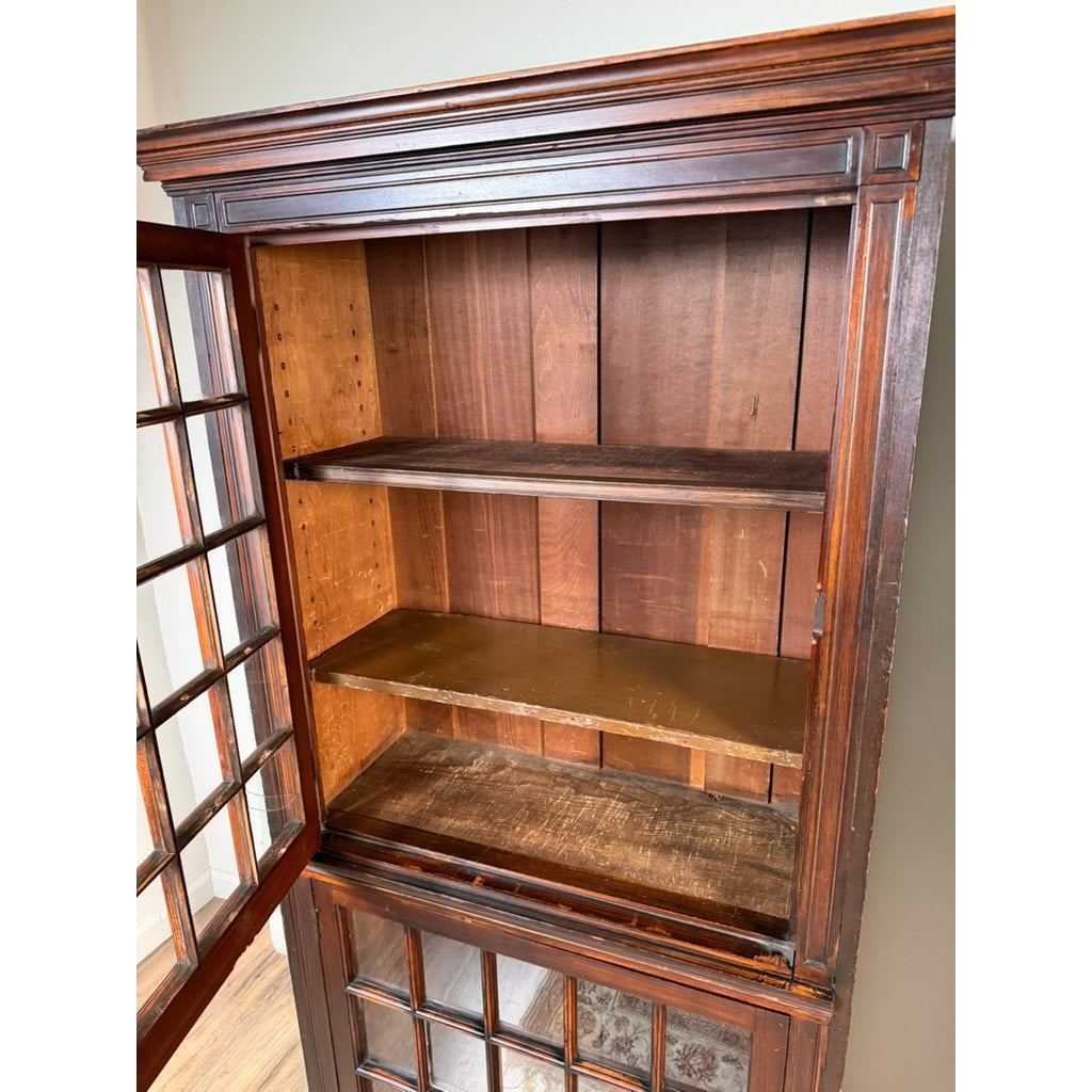 A pair of mid-19th century New England cherry glazed display cupboards by Pearl City Antiques, c. 1840–1860, featuring glass-paneled doors (the left door partially open) and three empty interior shelves. The wood exhibits visible age and wear, set against a light-colored wall.