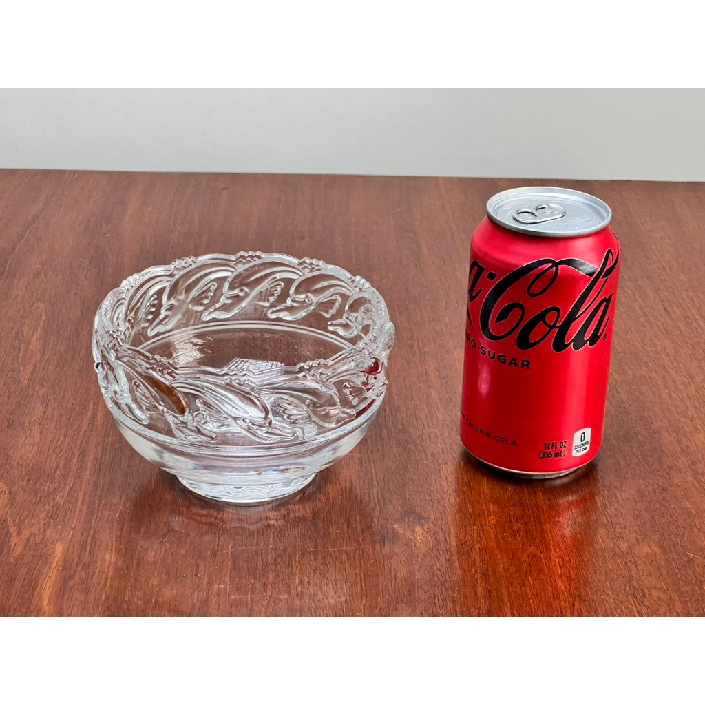 A red Coca-Cola can is placed beside a Tiffany & Co. Vintage Mid-Century Modern Crystal Dolphin Pattern Footed Bowl on a wooden surface.