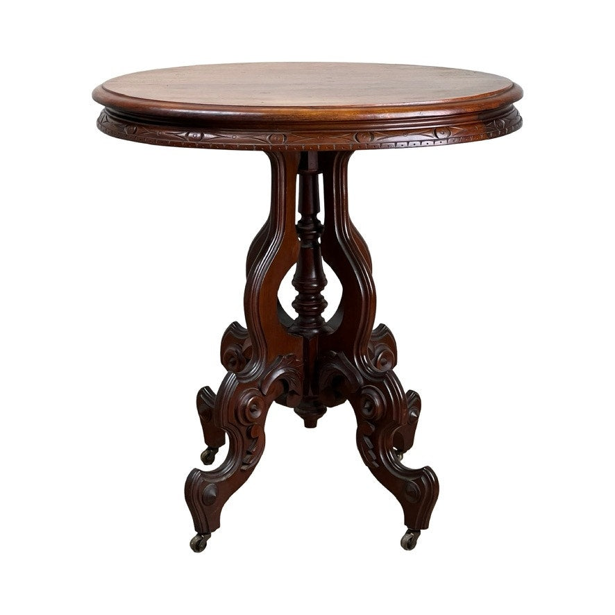This Antique Victorian Walnut Lamp Stand from the late 19th century features a round, ornately carved design with a polished surface atop an intricate pedestal base and curved legs with casters—a true period accent piece.