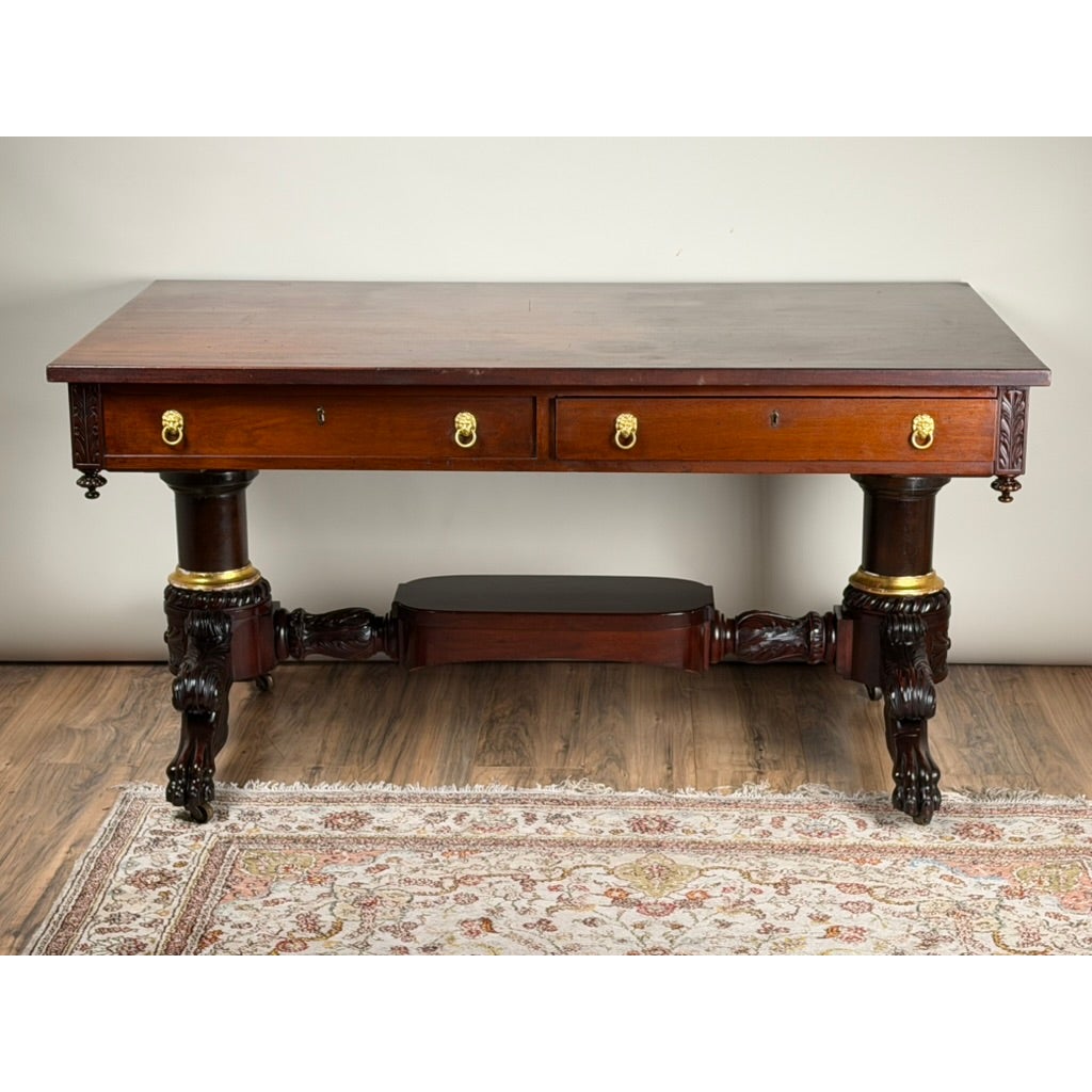 A New York Classical Revival Carved Mahogany Double-Pedestal Library Table, labeled Ernest F. Hagen, featuring a rectangular top, two drawers with brass lion-head pulls, and carved pedestal legs with claw feet.