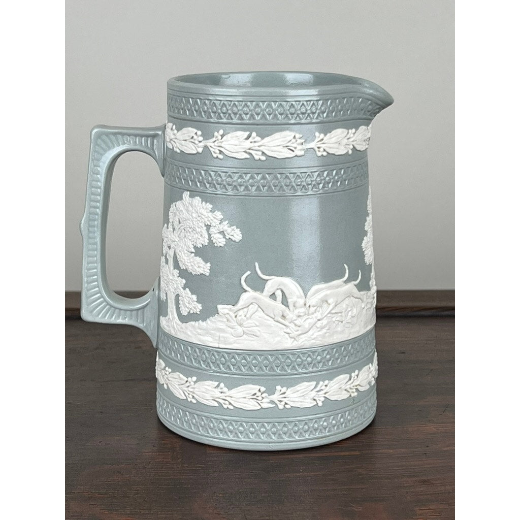 Vintage Copeland Spode English Jasperware Fox Hunt Pitcher in light blue, featuring white raised relief of animals and trees with ornate borders, large handle, and resting on a dark wooden surface.