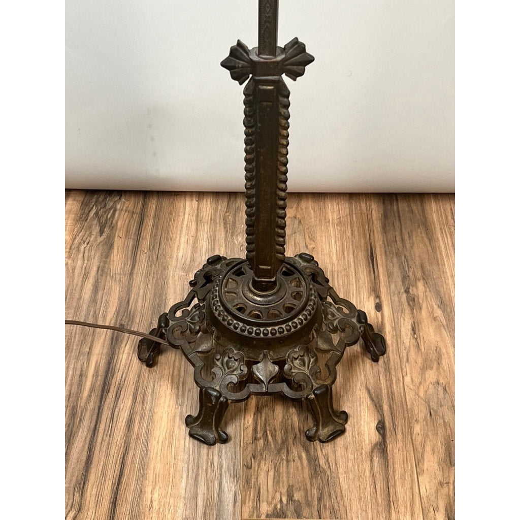 The Antique Art Deco Cast Iron Floor Lamp by Rembrandt features an ornate dark cast iron base with intricate patterns and four decorative legs, standing on a wooden floor with a power cord visible to the left.