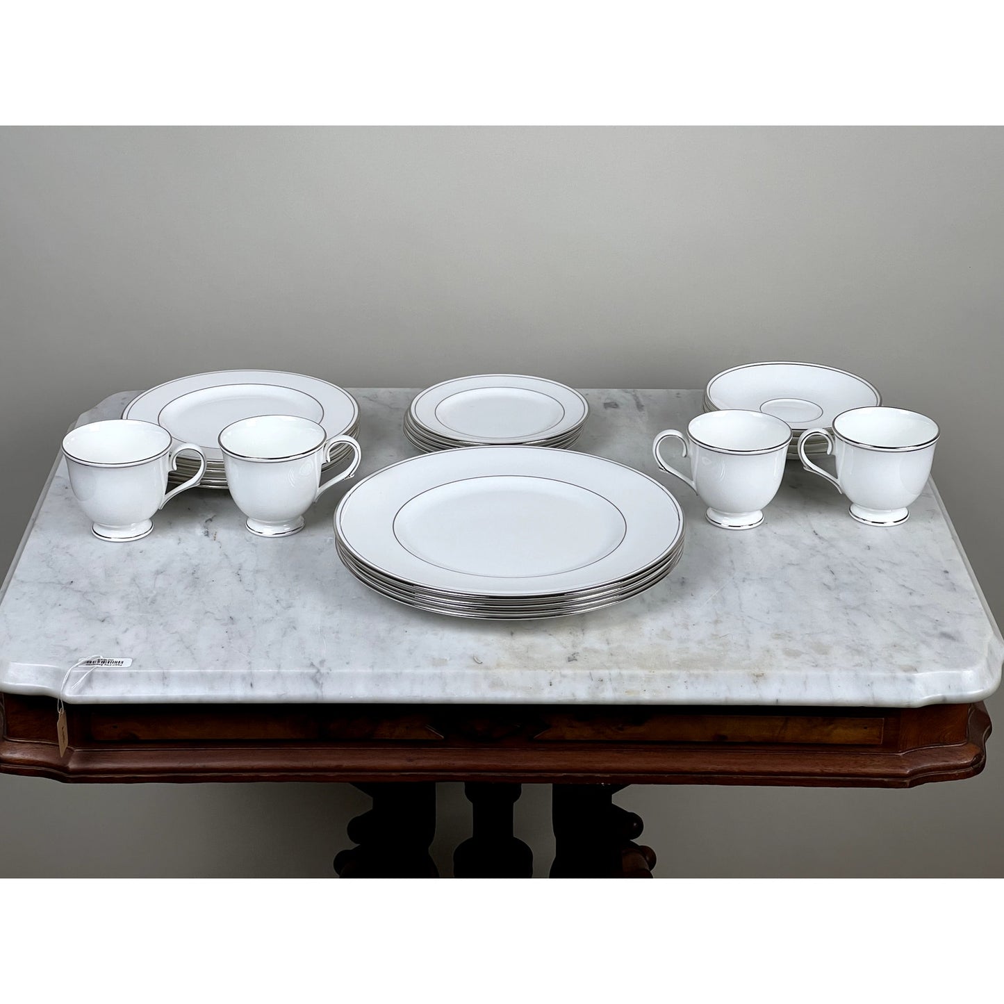A Vintage Lenox Federal Platinum Fine English Bone China Service for Four, featuring plates, bowls, and cups with silver rims by Lenox, arranged on a marble-topped wooden table against a plain background.