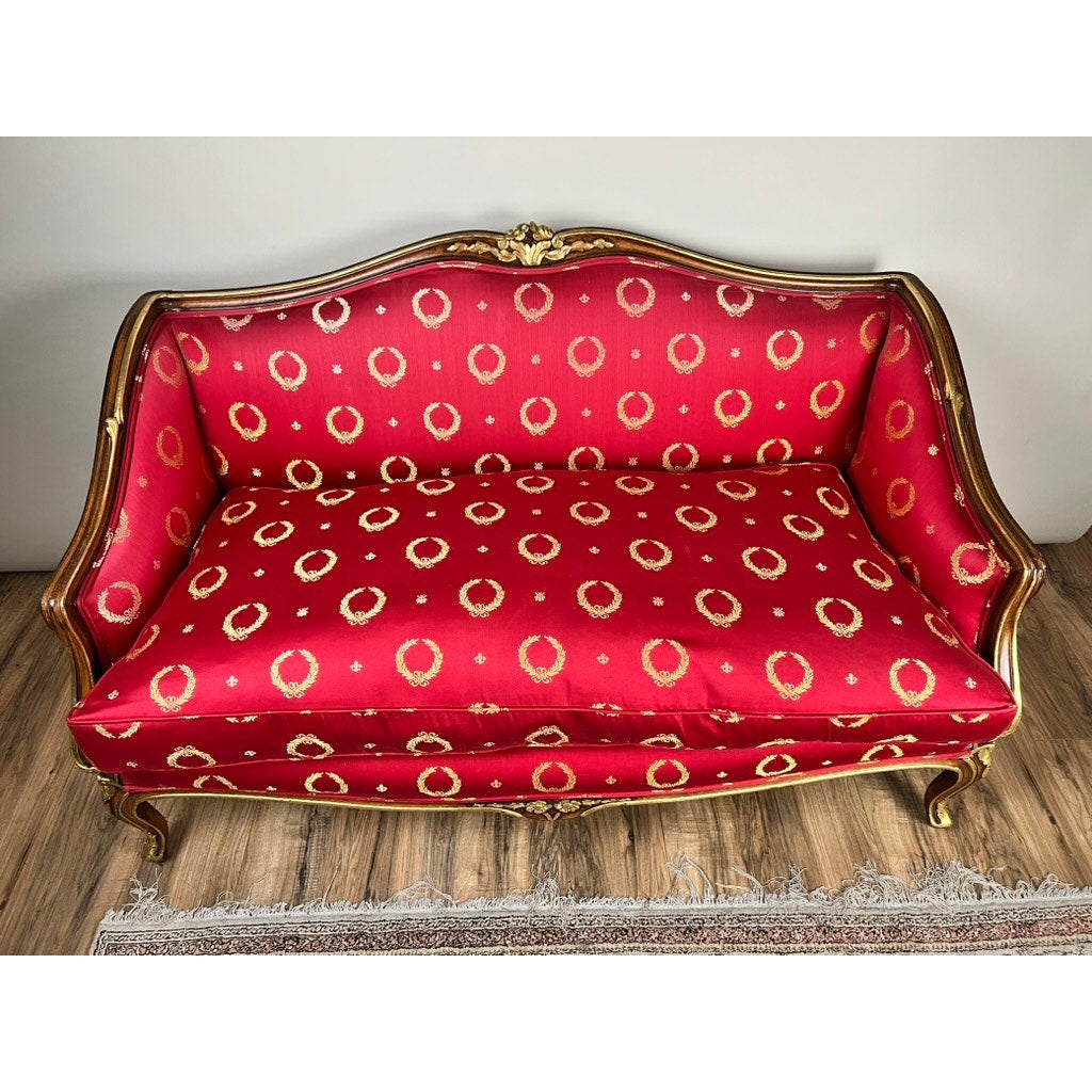 A Vintage French Regency Style Custom Upholstered Settee with red and gold circular fabric and a giltwood frame stands on a wooden floor next to a fringed rug.