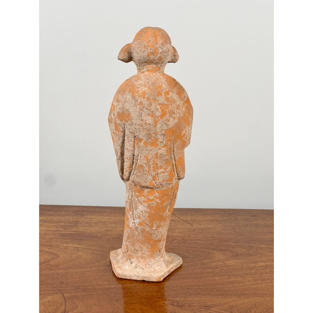 An Antique Chinese Tang Dynasty (618-907 AD) terracotta figure of a standing court lady with COA stands on a wooden surface, her rounded head and simple robe echoing early Chinese art against a plain light background.