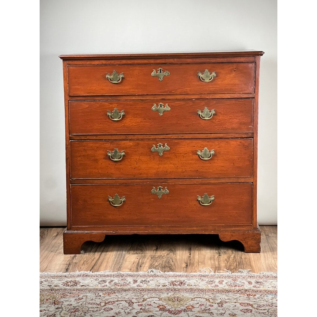 An Antique Chippendale Pine Graduated Four Drawer Chest, attributed to a late 18th-century Northampton MA maker, features brass handles and a warm reddish-brown finish. It rests on a wood floor with part of a patterned rug visible in front.