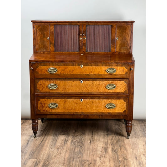 Antique Federal Period Tambour Secretary in Mahogany and Birdseye Maple, c. 1800 by Pearl City Antiques, featuring intricate mahogany grain patterns and elegant birdseye maple accents, brass hardware, and turned legs—an exceptional example of early American craftsmanship—displayed on a wood floor against a plain light gray wall.