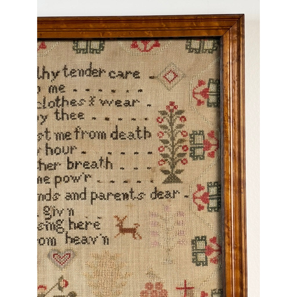 A close-up of an Exceptional English Regency Schoolgirl Needlework Sampler by Charlotte Rees, age 11 and dated 1816, features text, floral patterns, a small deer, and geometric shapes on a beige background. The wood frame is visible along the left and top edges, highlighting this remarkable early 19th-century piece.