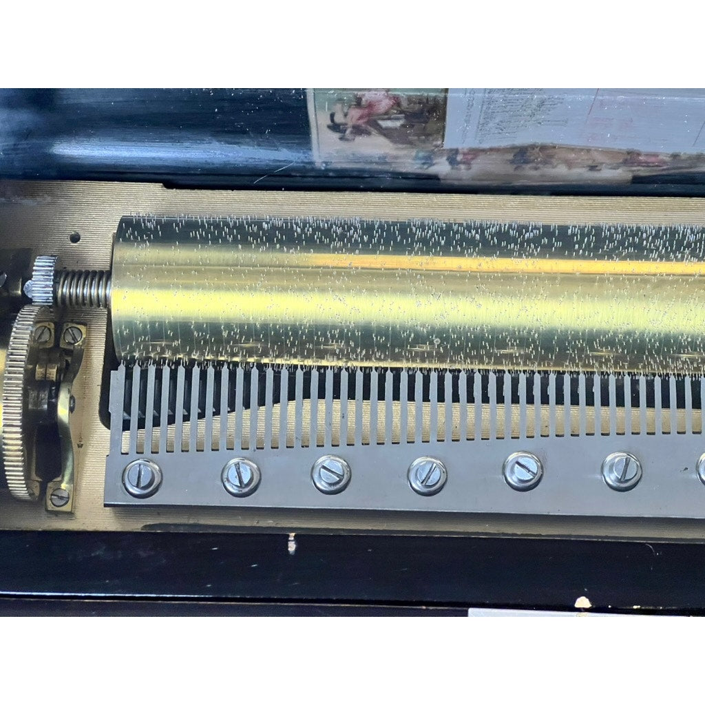 Close-up of the Antique Swiss 12 Tune Music Box (c. late 19th century) mechanism, with a brass cylinder and metal comb that play melodies as the cylinder rotates; brand unknown.